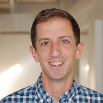 A man with a blue plaid shirt and a smile on his face.