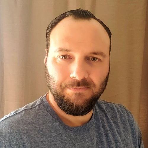 A man with a beard and mustache wearing a blue shirt.
