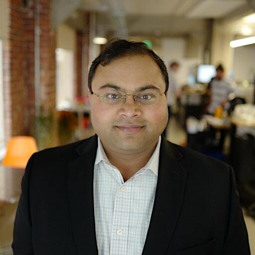 A man wearing a suit and glasses is smiling.