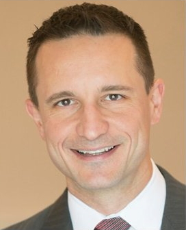 A man wearing a suit and tie smiling for the camera.