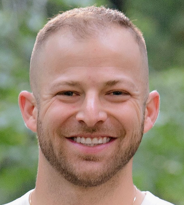 A man with a shaved head smiling for the camera.