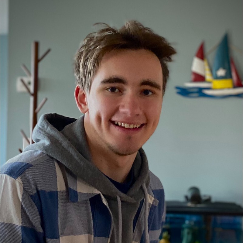 A man wearing a plaid shirt and a gray hoodie smiles for the camera.
